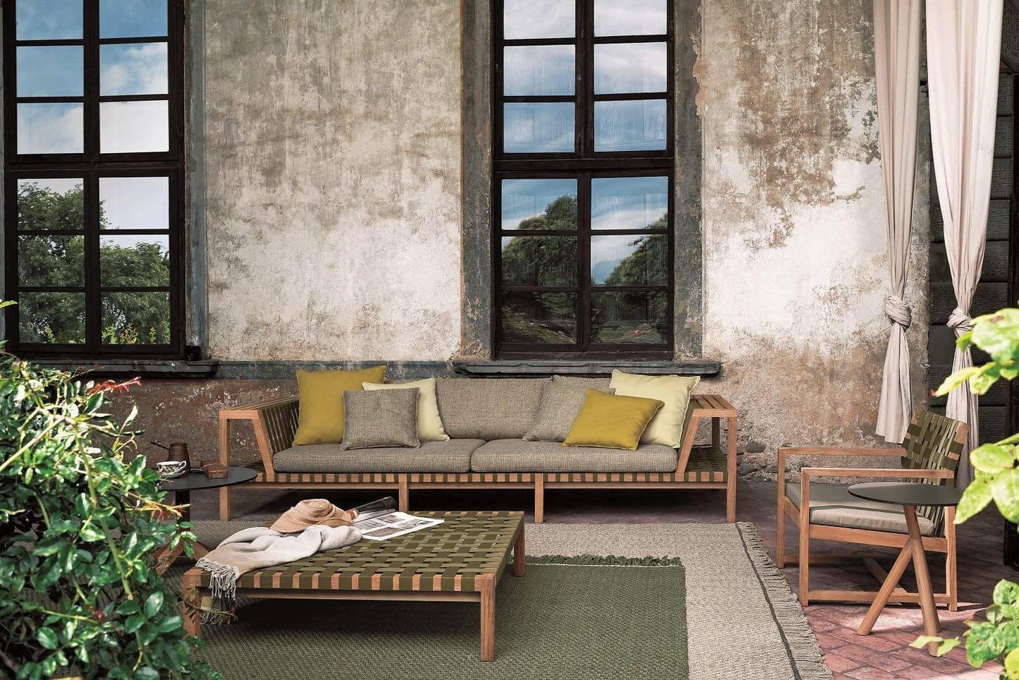 Outdoor seating area with a sofa, coffee table, and chairs against a textured wall with large windows.