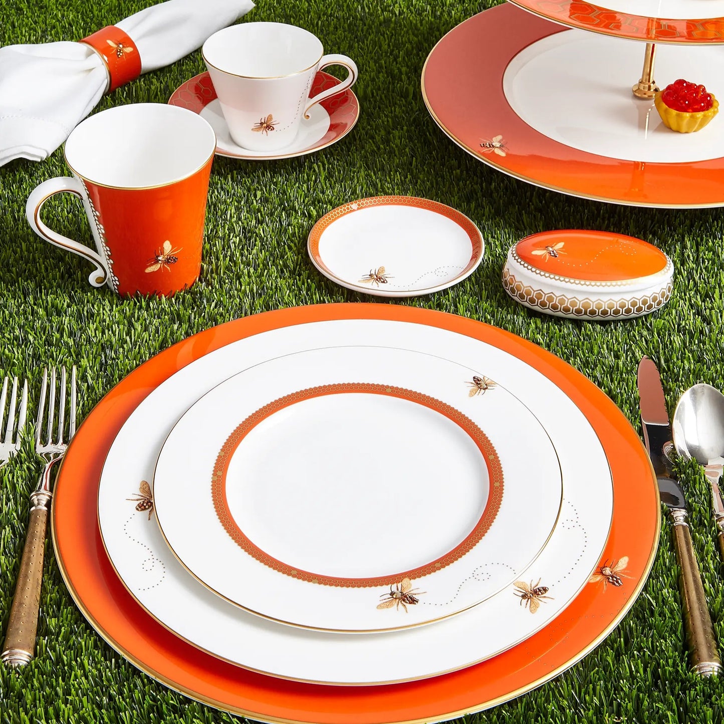 Dining set with orange and white plates, cups, and cutlery on grass