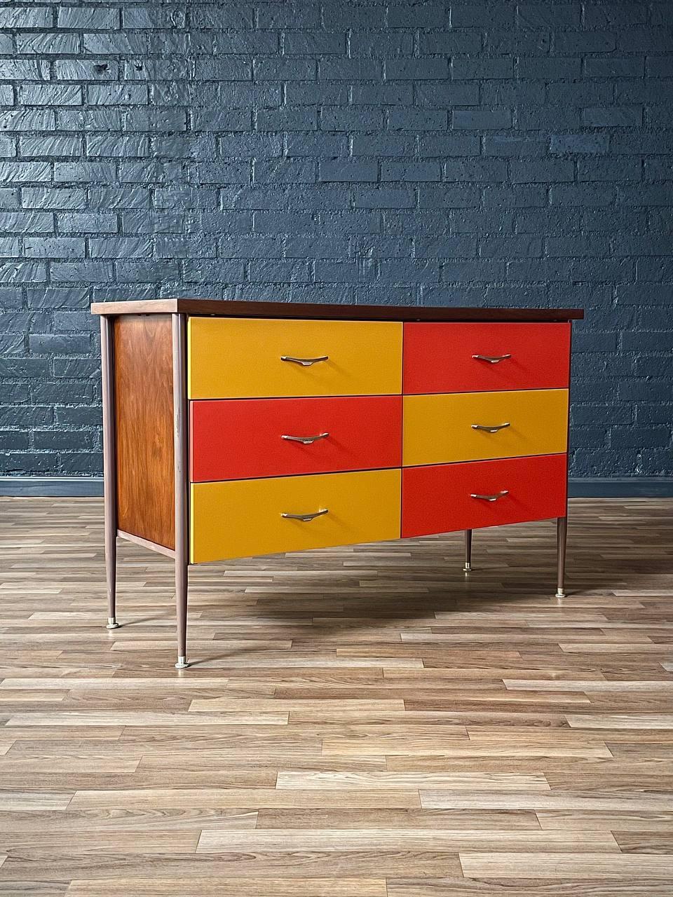 Colorful dresser with wooden frame against a blue brick wall.