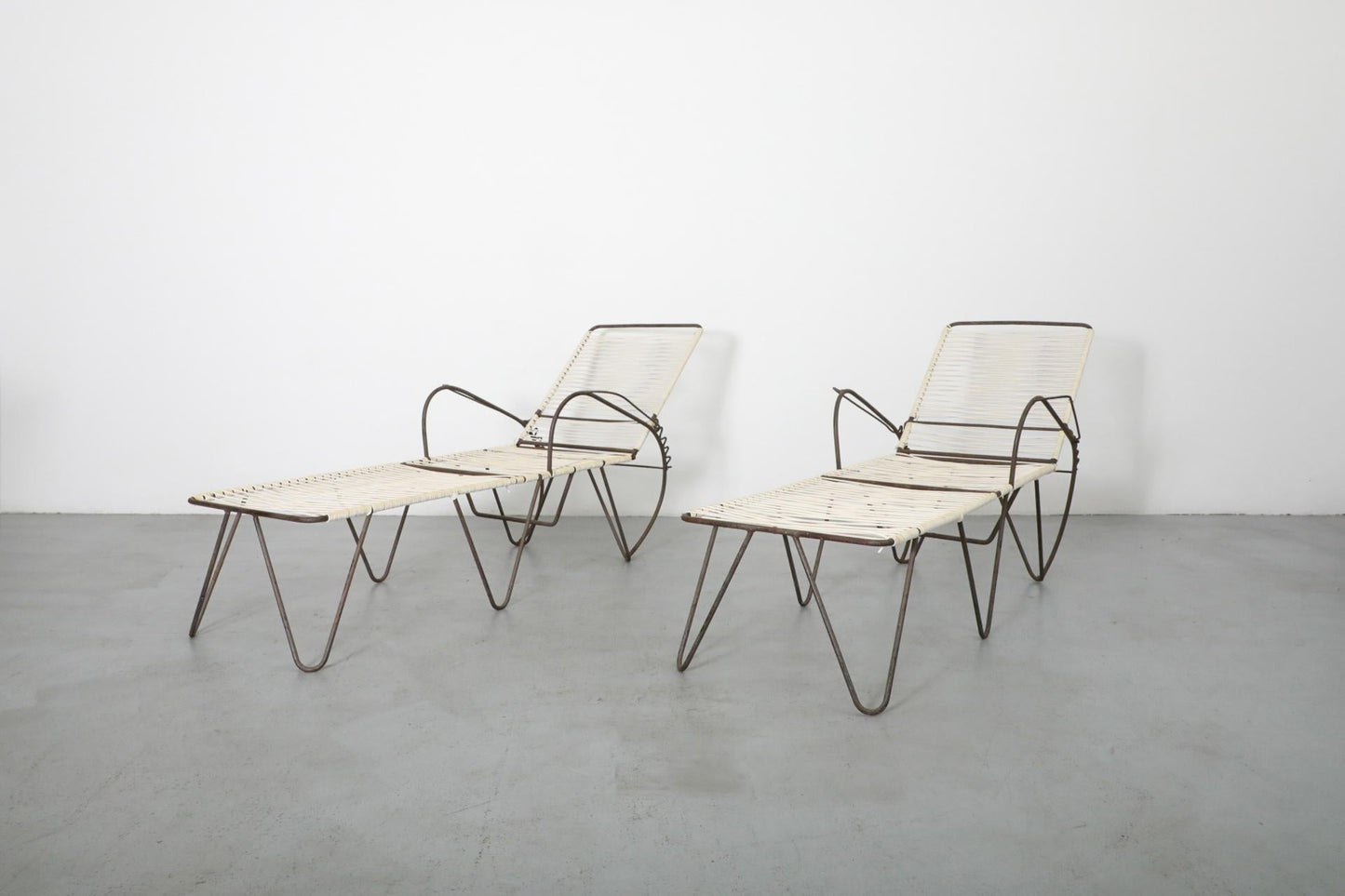Two modern chairs with ottomans on a gray floor against a white wall