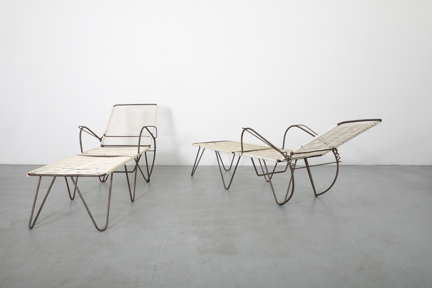 Two modern lounge chairs with metal frames and woven seats on a gray floor.