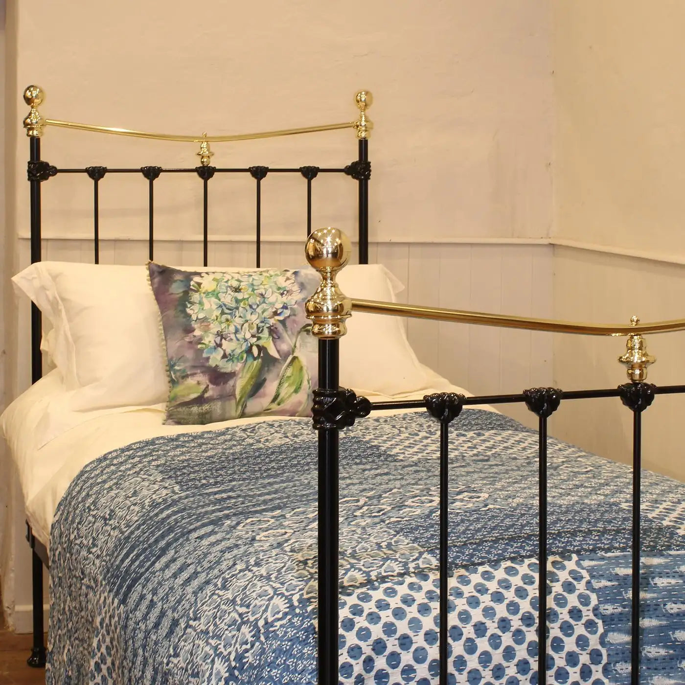 Bed with decorative pillows and a blue patterned quilt, featuring a brass headboard.