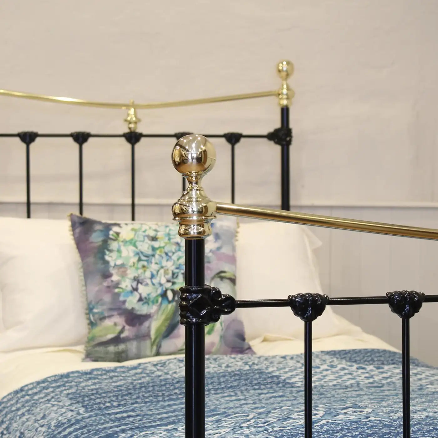 Close-up of a black metal bed frame with gold accents and pillows in the background.