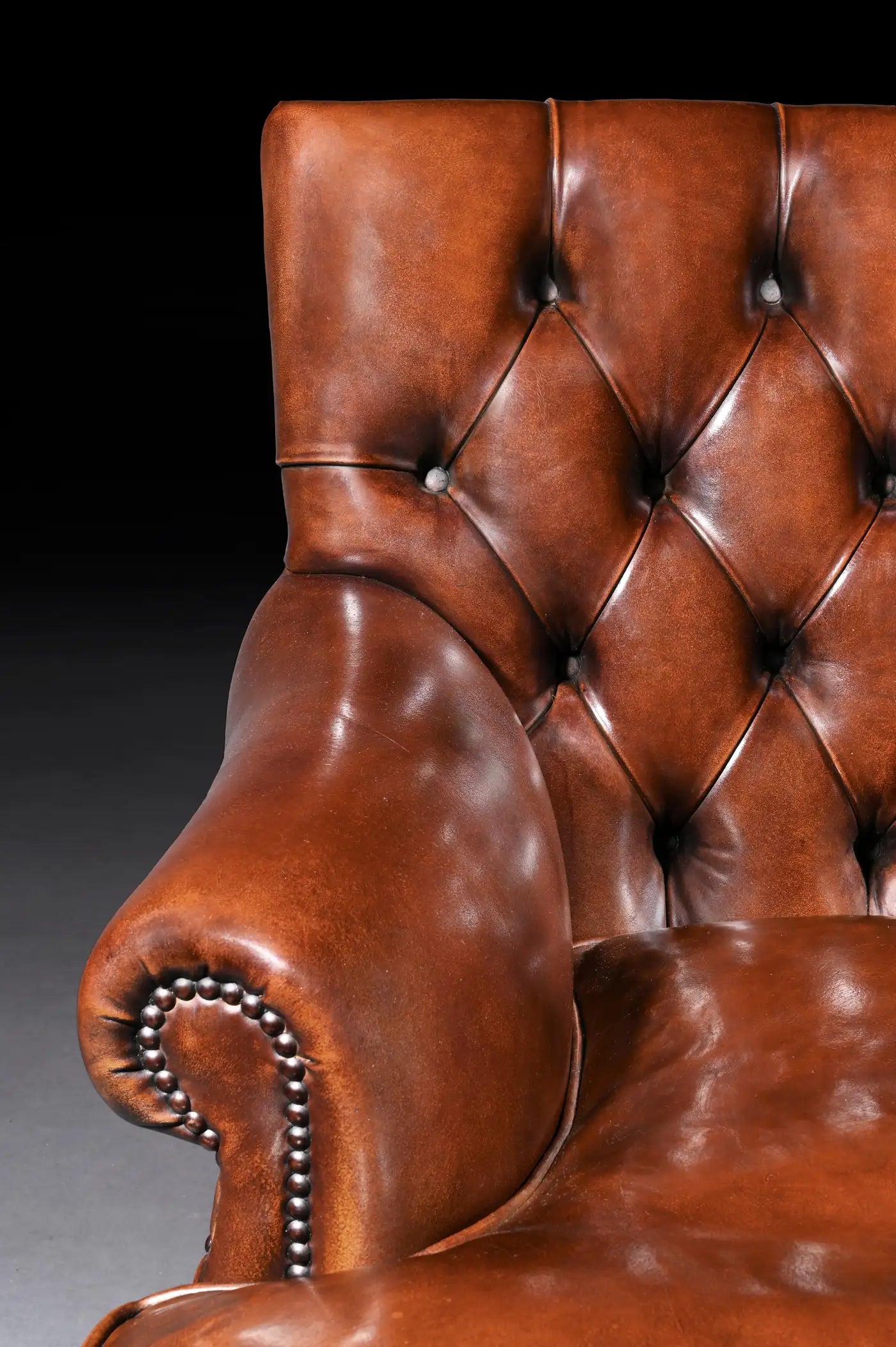Close-up of a brown leather armchair with buttoned backrest on a dark background