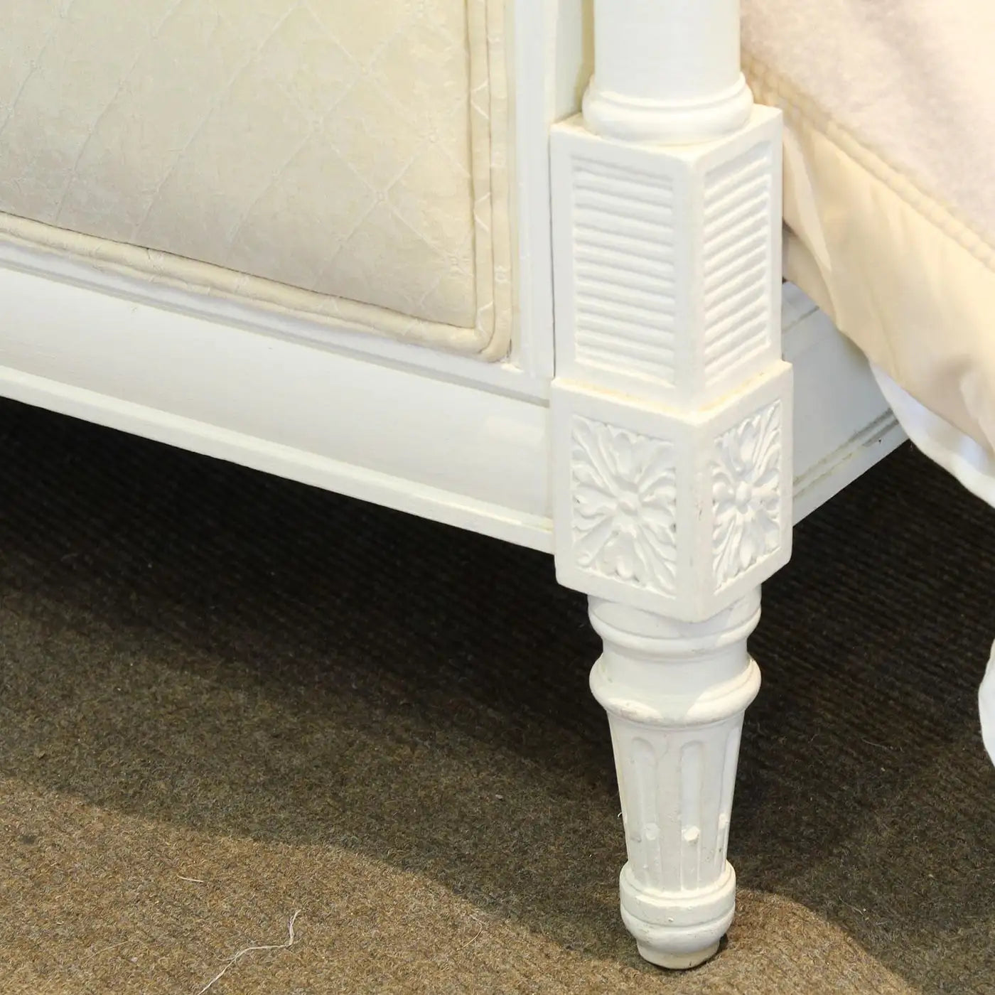 Close-up of a white wooden furniture leg with decorative carvings on a carpeted floor.