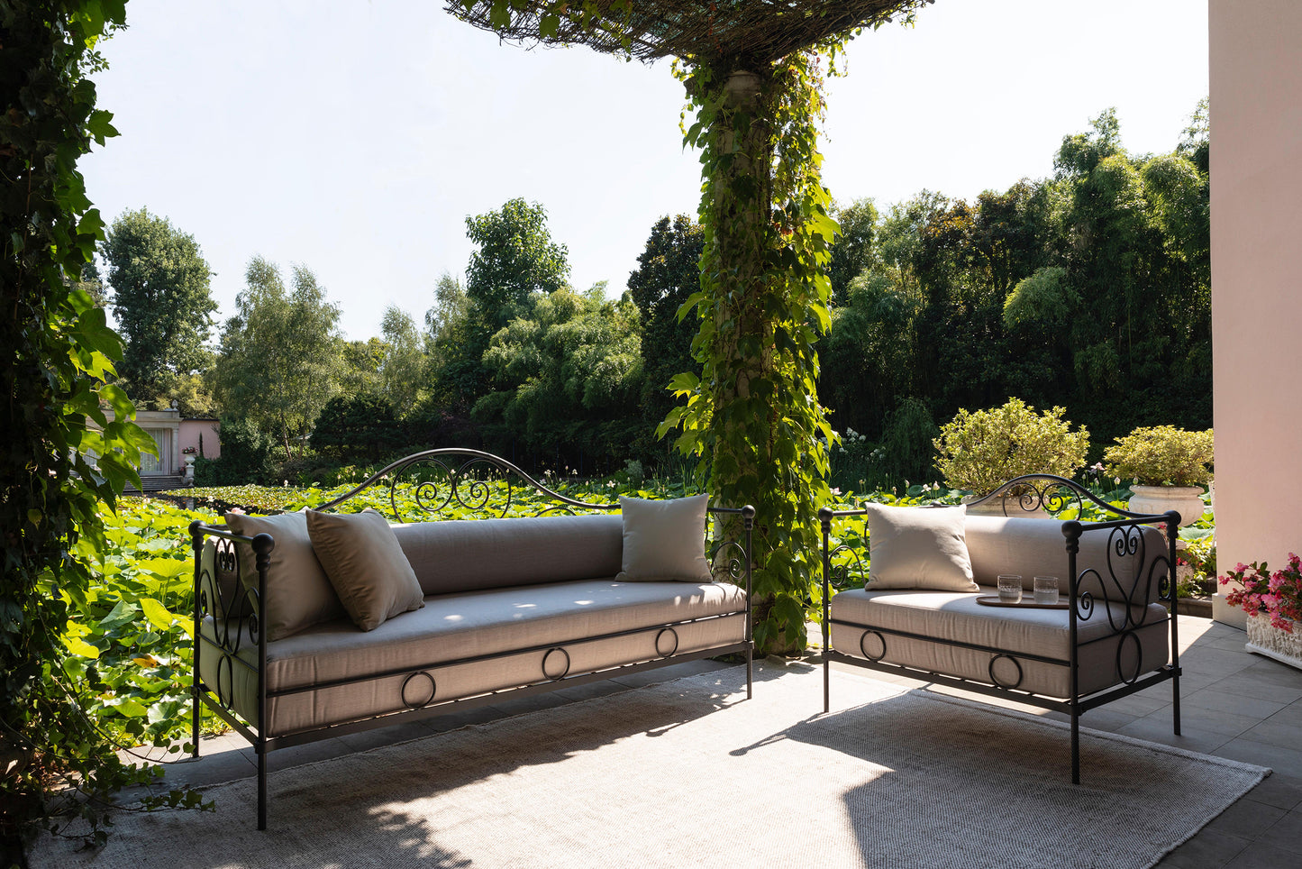 Outdoor patio with two metal sofas and cushions, surrounded by greenery.