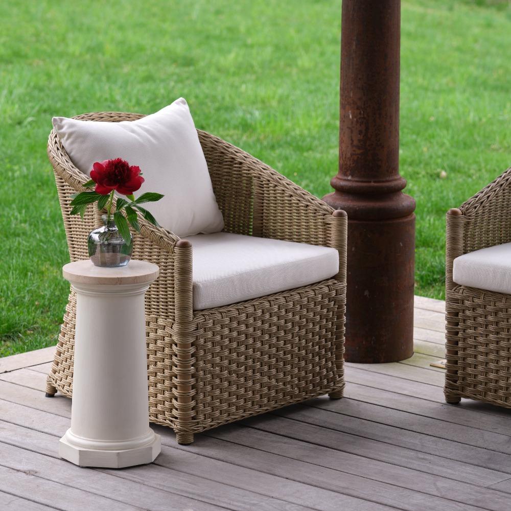 Wicker chair with white cushion and small table with red flowers on a wooden deck.