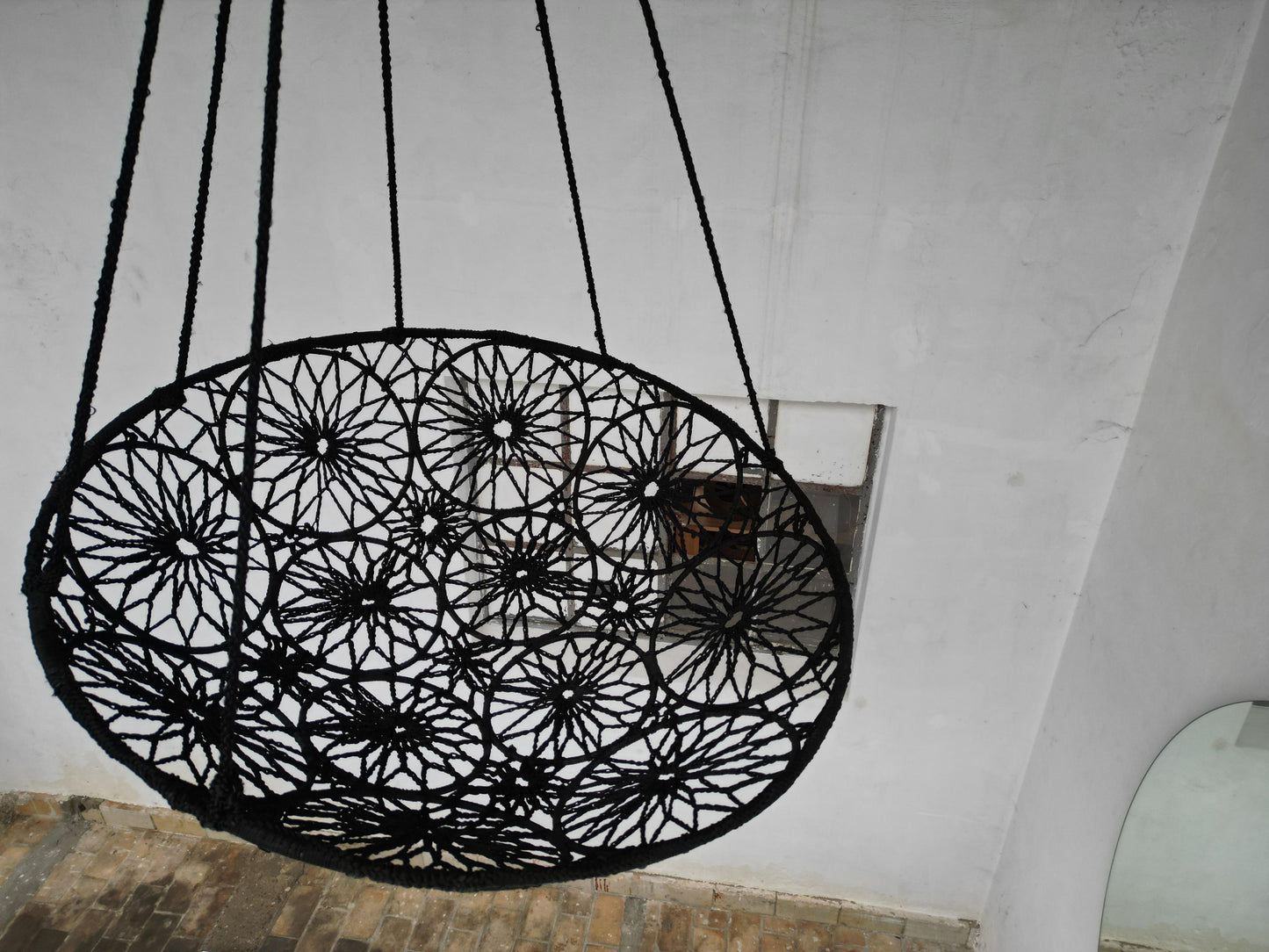 Black woven chair hanging from the ceiling against a white wall.