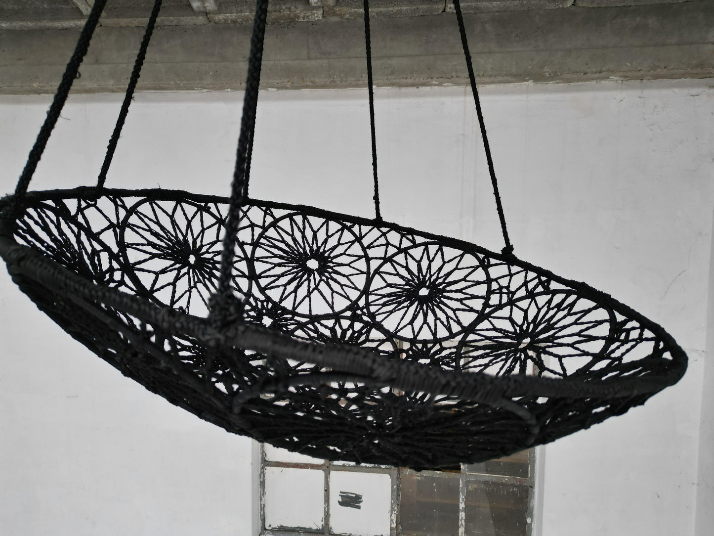 Black woven swing hanging against a white wall.