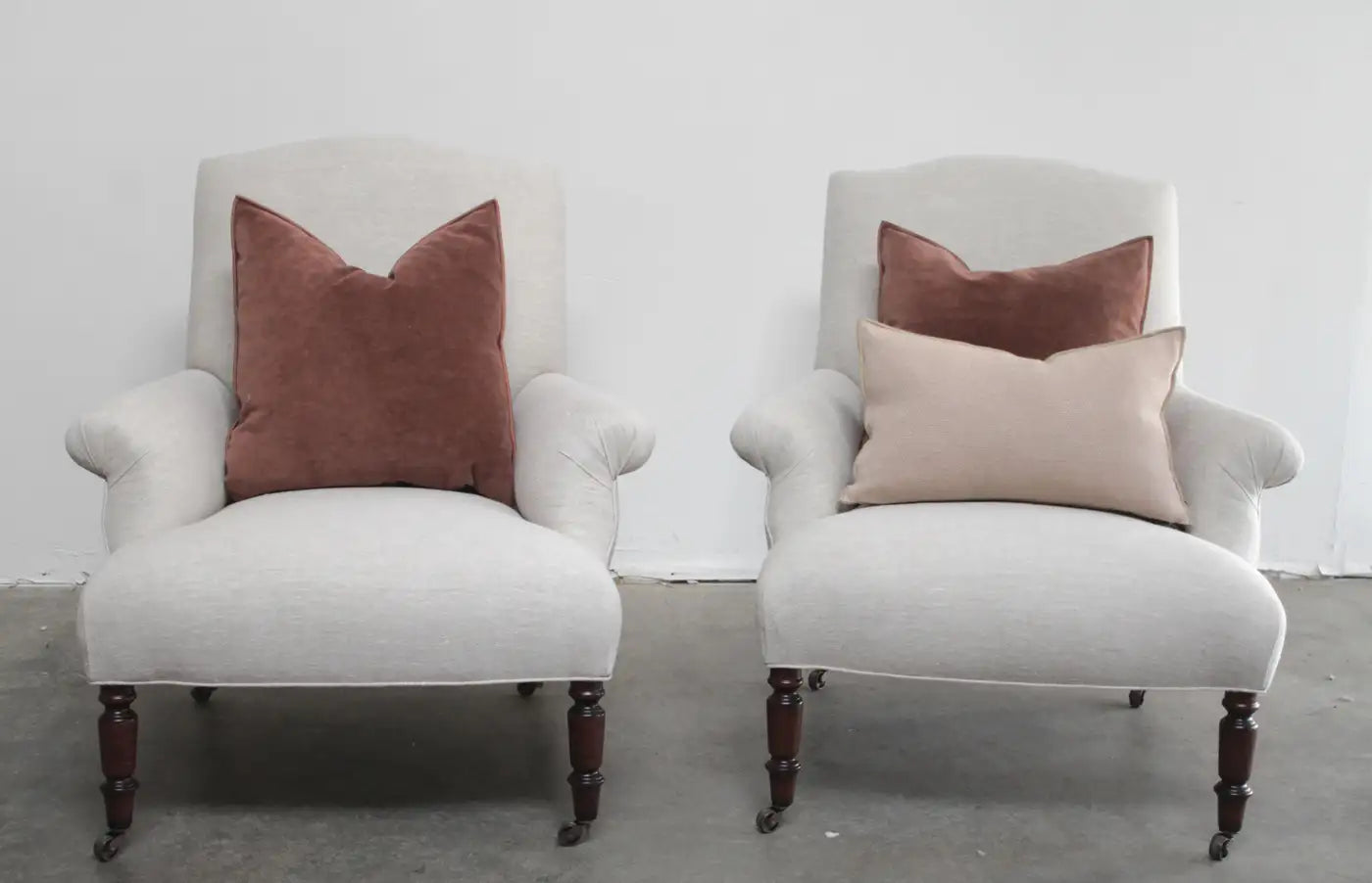 Two white armchairs with brown and beige cushions on a gray floor.