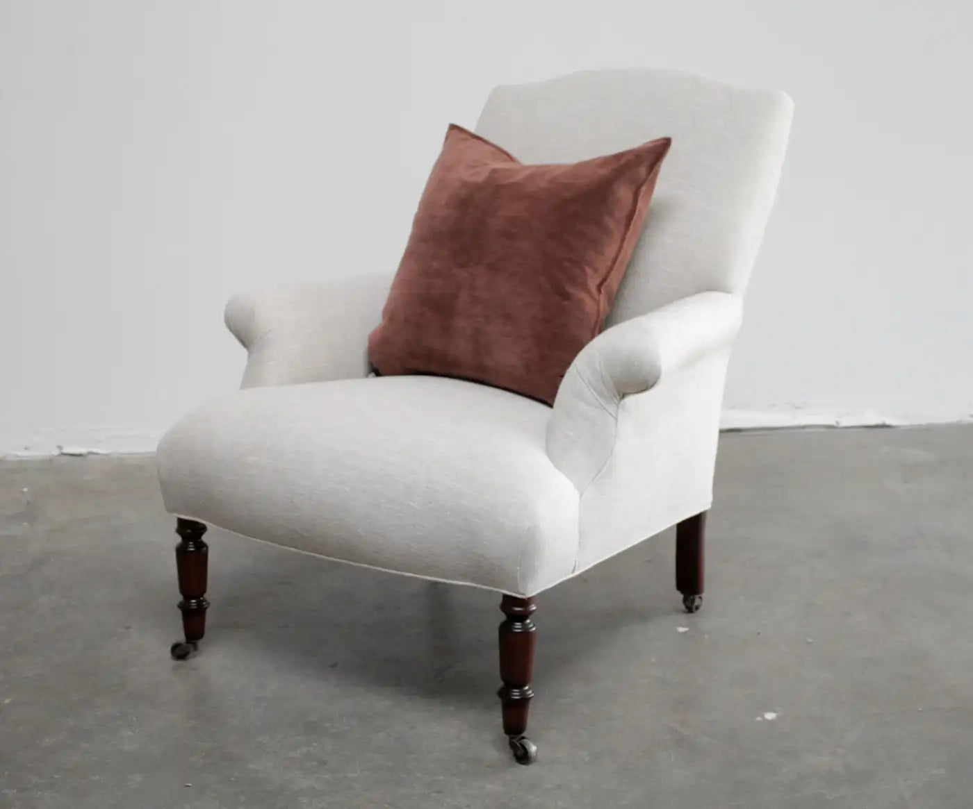 White armchair with a brown pillow on a gray floor against a white wall