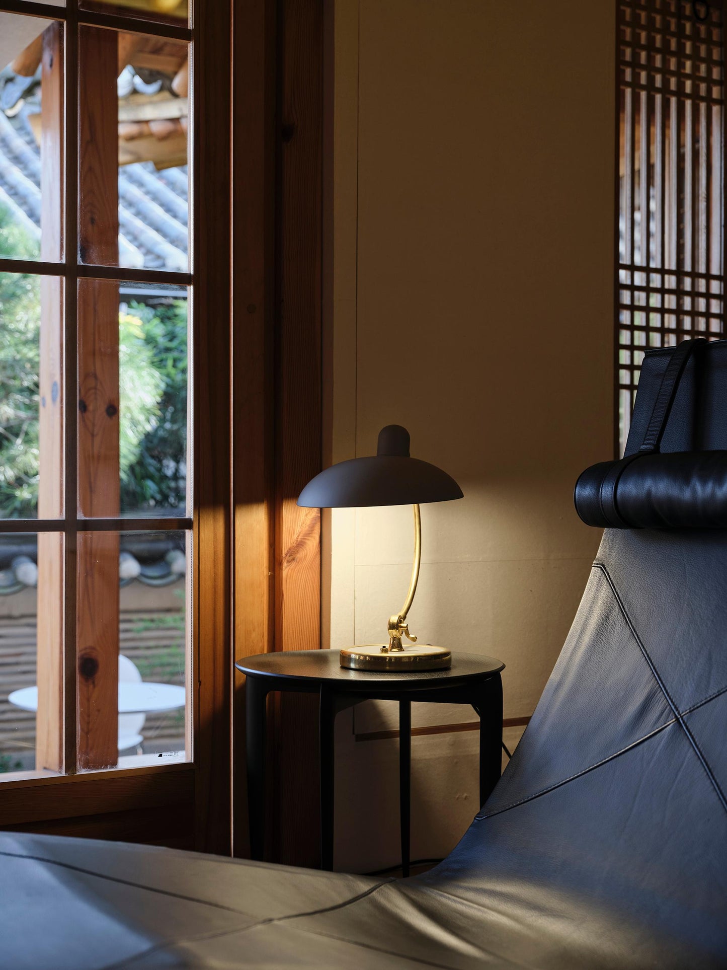 Modern interior with a lamp on a side table next to a window with wooden frames.