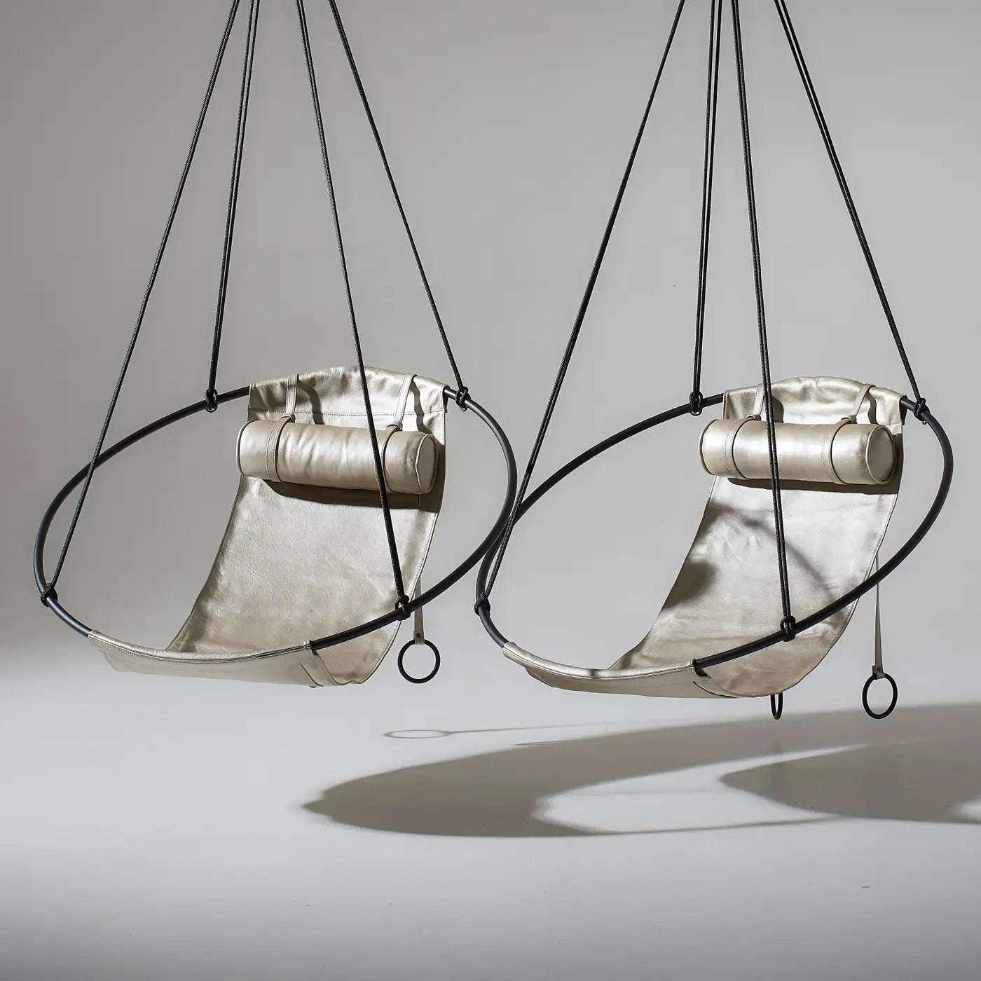 Two metallic hanging chairs with black straps on a gray background