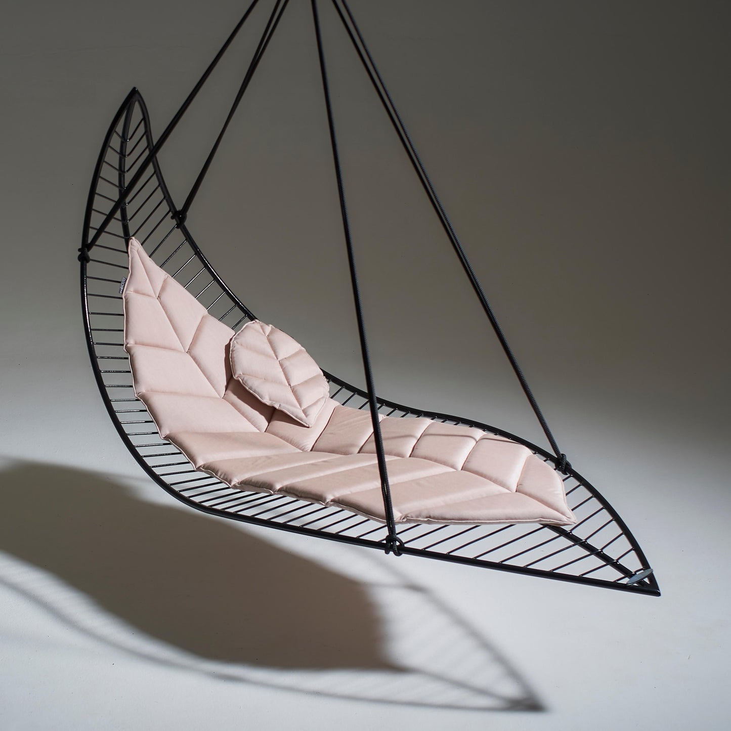Hanging chair with pink cushion in the shape of a leaf on a neutral background
