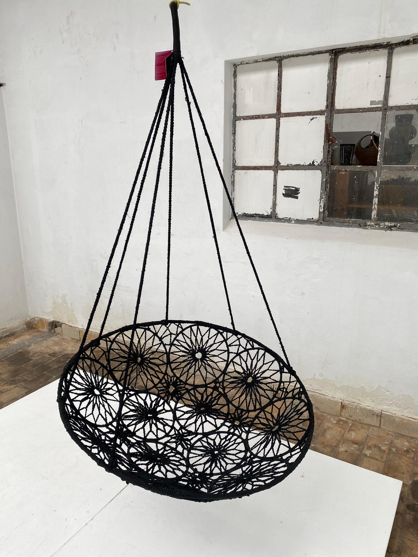 Black woven hanging chair in a room with a window and wooden floor.
