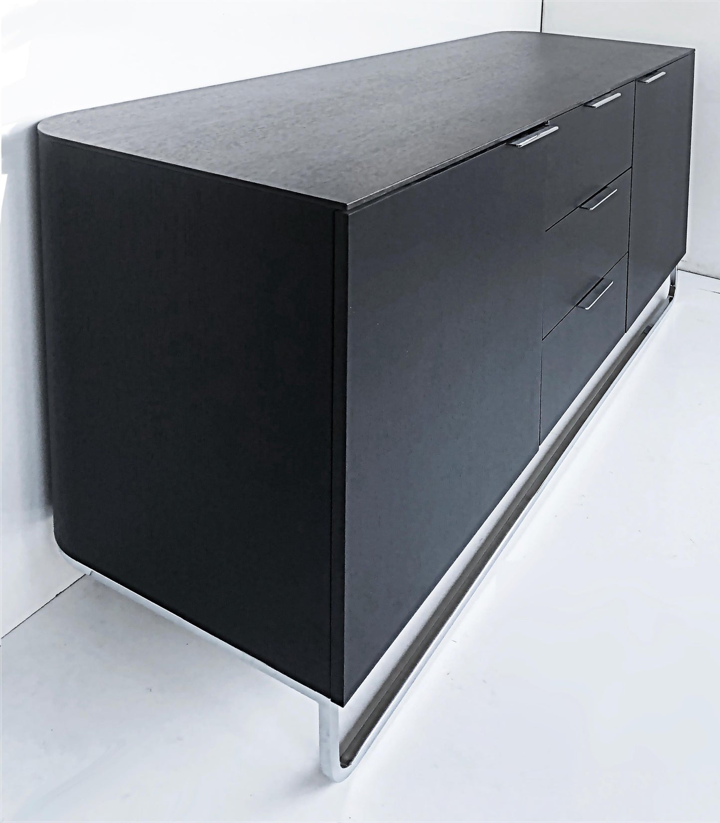 Black sideboard with drawers on a white floor and wall