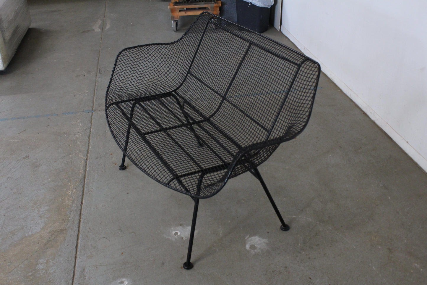 Black wire mesh chair on a concrete floor with a white wall in the background