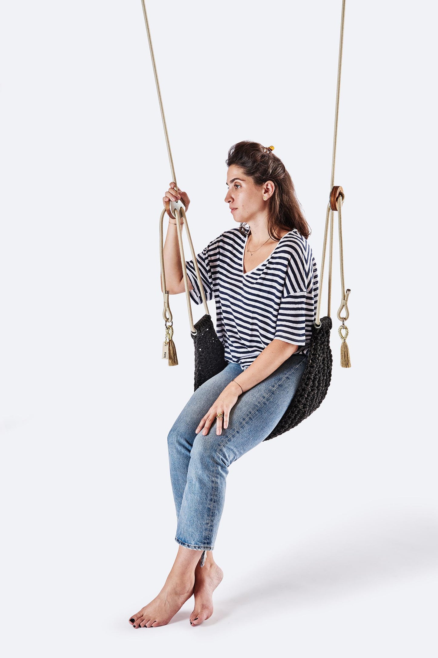 Woman sitting on a black woven swing against a white background