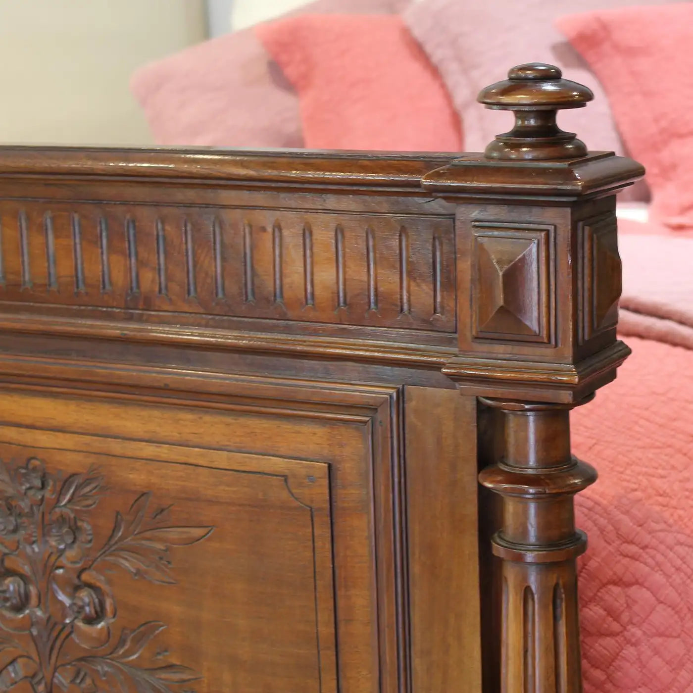 Close-up of a wooden headboard with intricate carvings against a pink textured background.