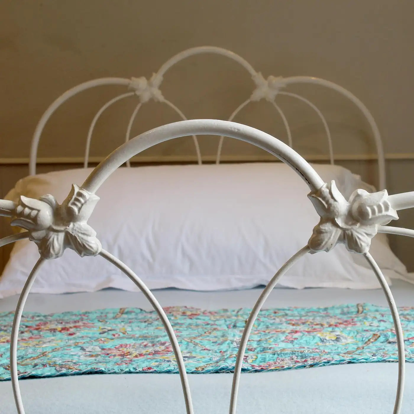 White metal bed frame with floral bedding and pillows against a beige wall.