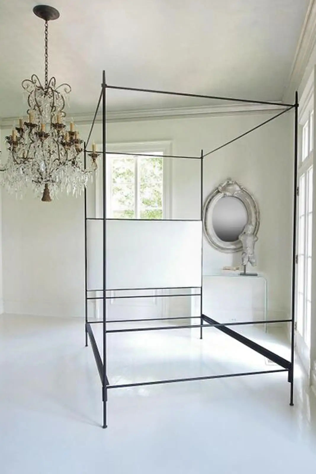 Black metal canopy bed in a bright bedroom with a chandelier and mirror.