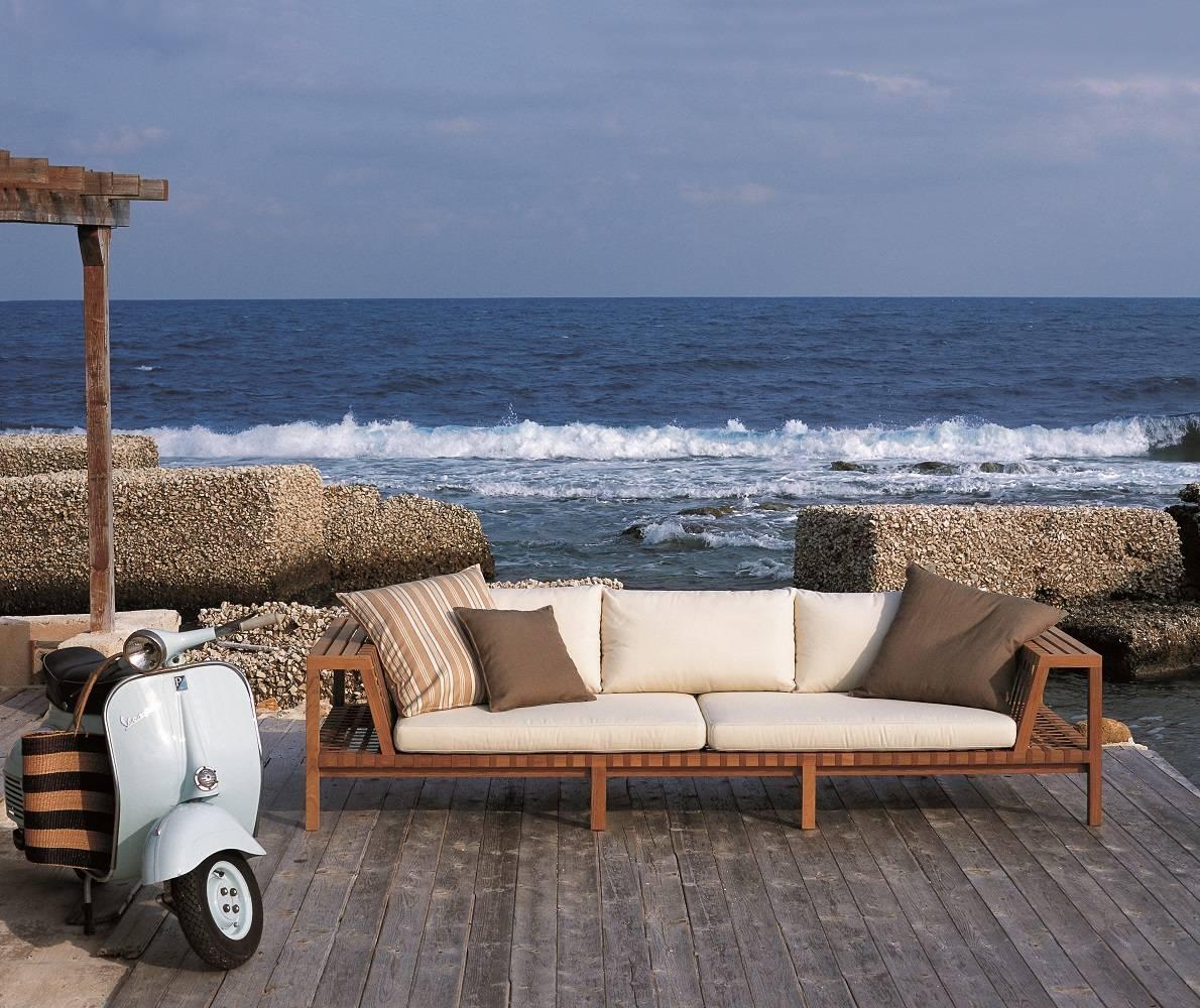 Wooden outdoor sofa with cushions on a deck overlooking the ocean.