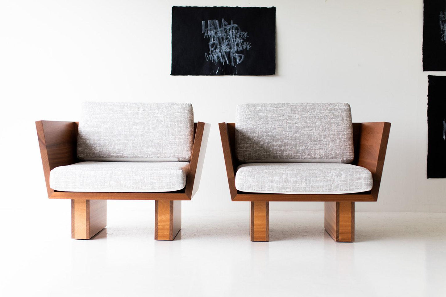 Two modern chairs with wooden frames and gray cushions in a minimalistic room.