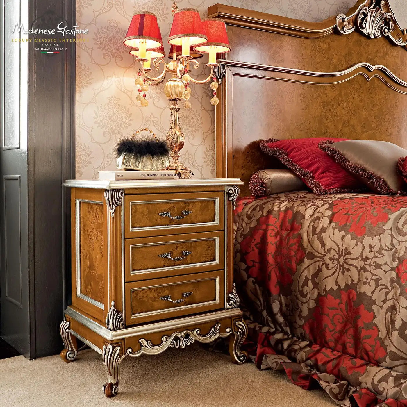 Luxurious bedroom with ornate nightstand and bed, featuring red and gold colors.