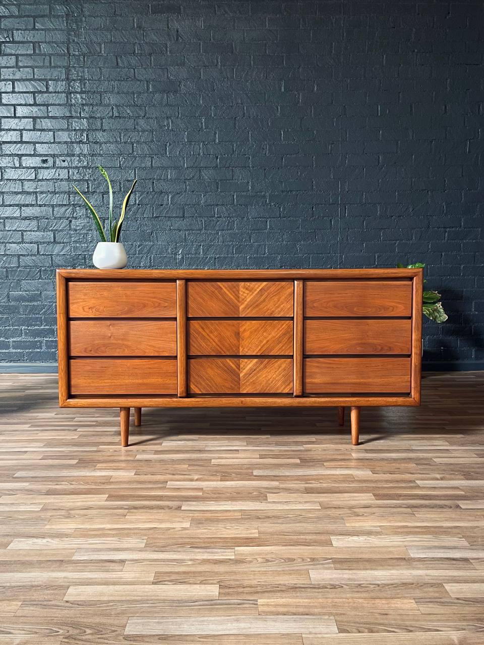 Wooden dresser against a dark brick wall with a plant on top