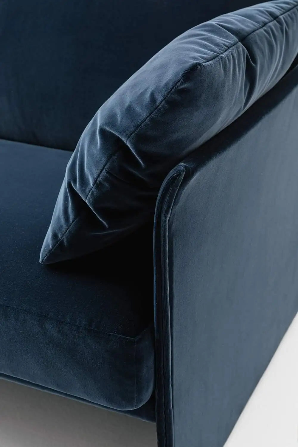 Navy blue velvet sofa with a pillow on a neutral background