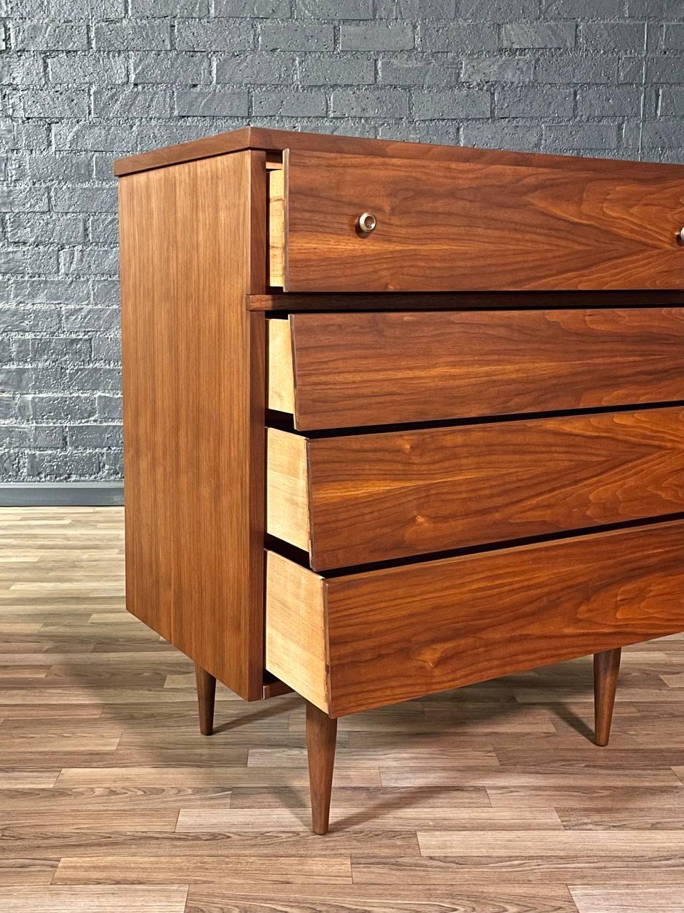 Wooden dresser with three drawers against a gray brick wall.