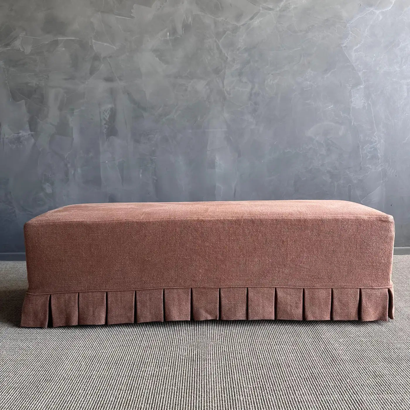 Brown ottoman with pleated design against a gray textured wall.