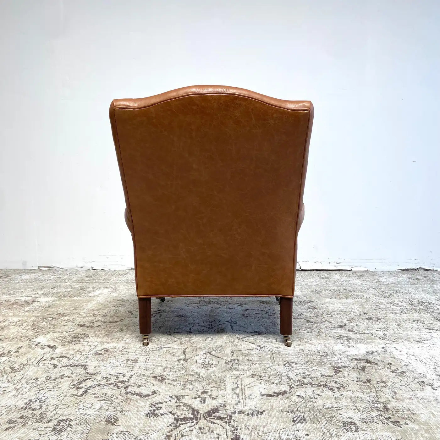 Brown leather armchair on a textured floor with a white wall background
