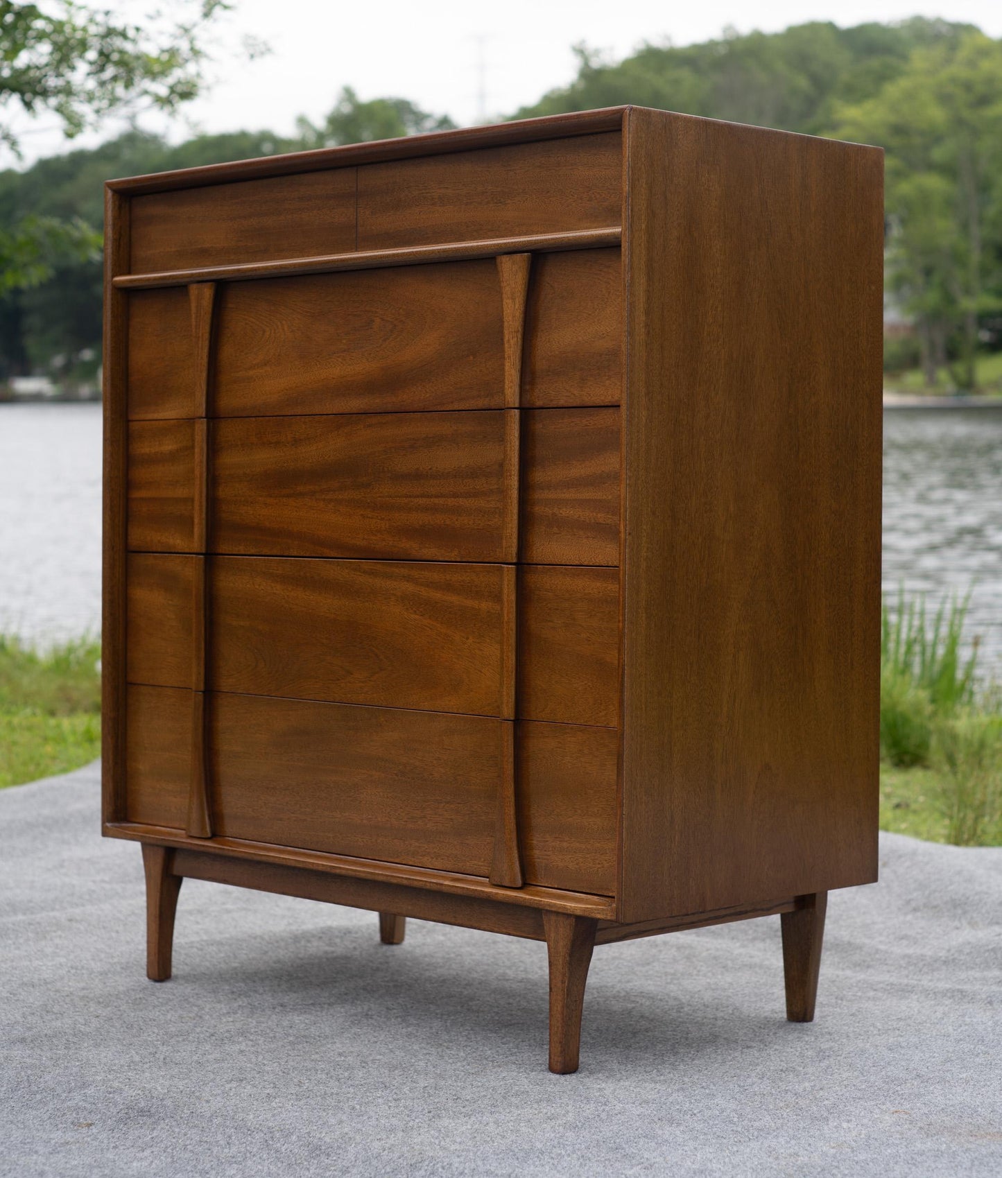 Wooden dresser with multiple drawers outdoors near a body of water
