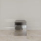 Modern side table with metallic finish in a room with light-colored walls and floor.