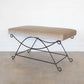 Beige ottoman with black metal frame on a light wooden floor.