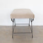 Beige ottoman with metal legs on a wooden floor against a white wall