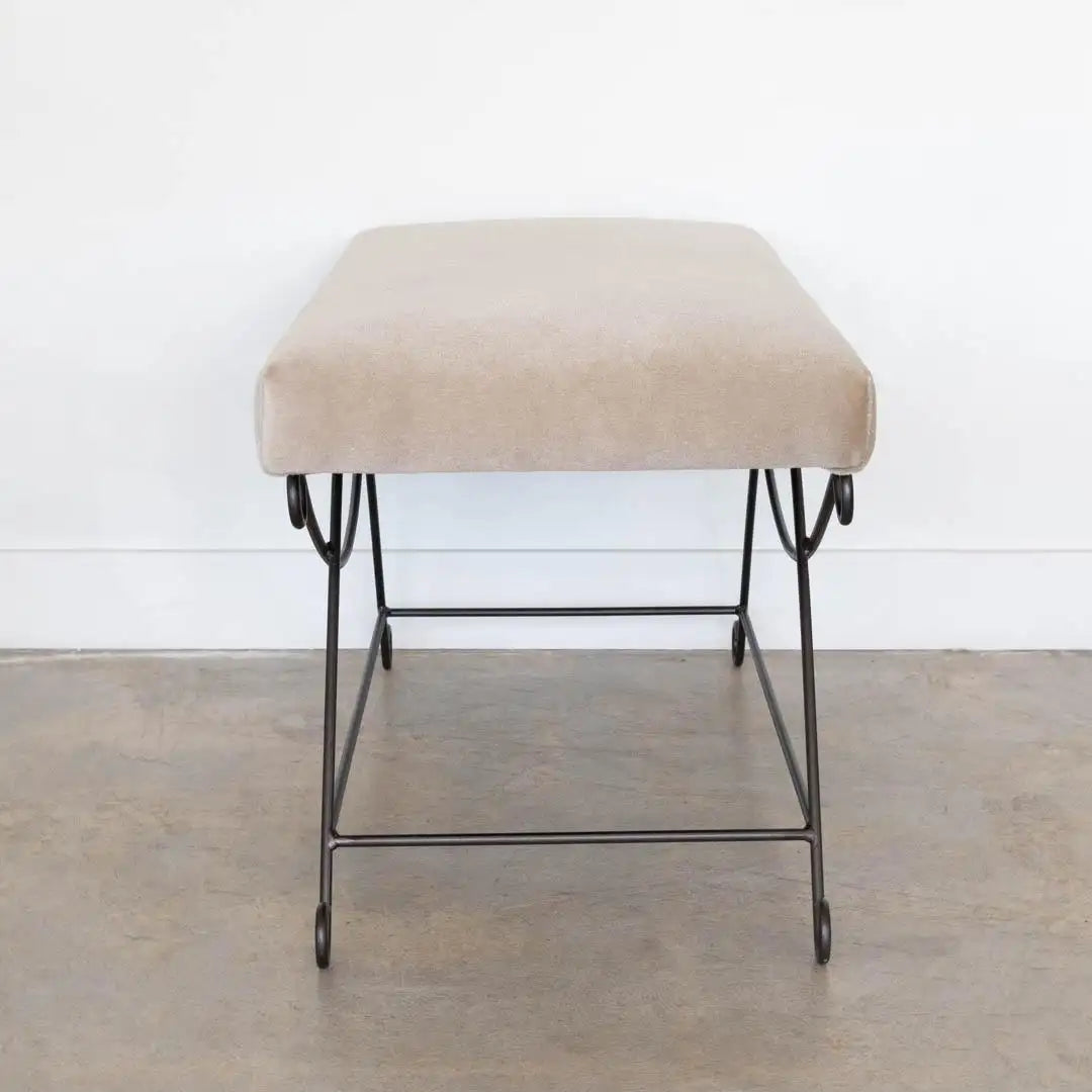 Beige ottoman with metal legs on a wooden floor against a white wall