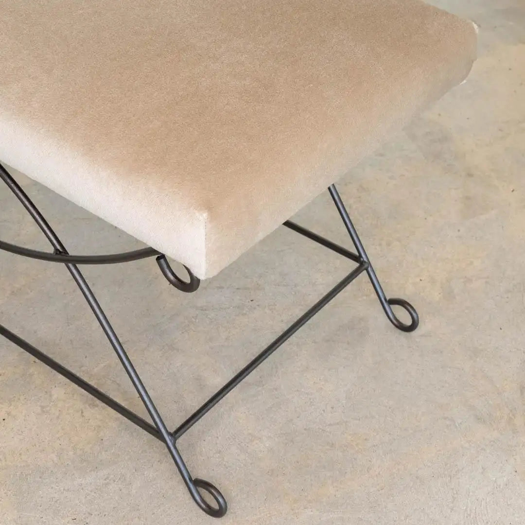 Beige cushioned stool with black metal legs on a concrete floor