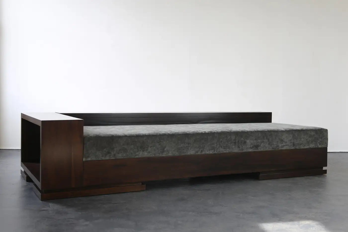 Modern bed with dark wooden frame and gray mattress on a plain background