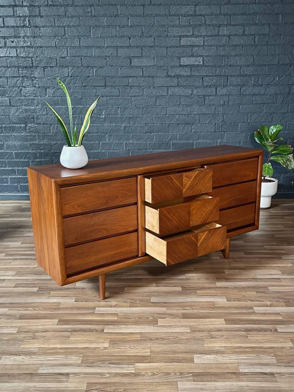 Wooden dresser with multiple drawers against a brick wall.