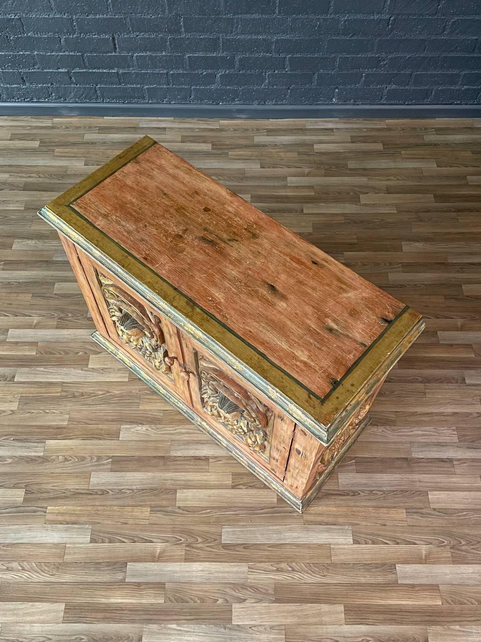 Wooden chest with decorative carvings on a wooden floor against a blue brick wall.