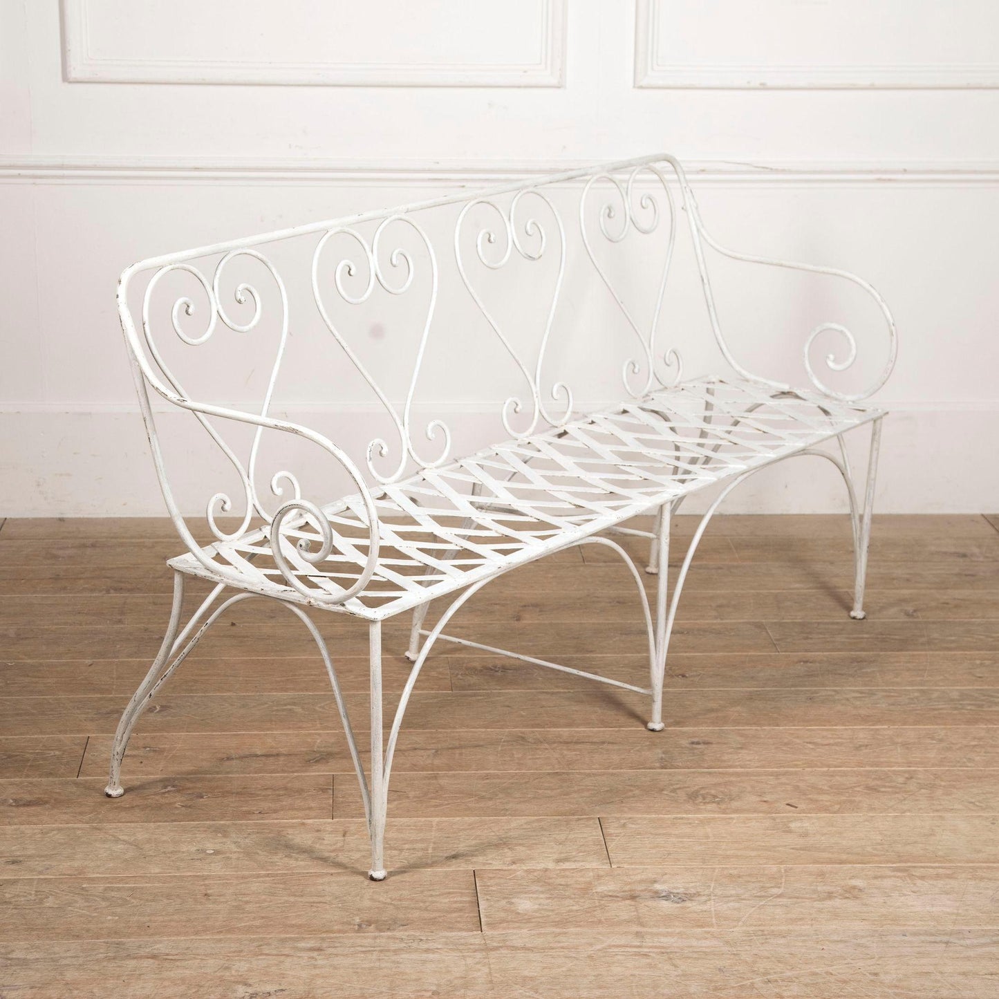 White metal bench with decorative backrest on a wooden floor