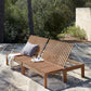 Wooden outdoor lounge chair with cushions on a stone patio