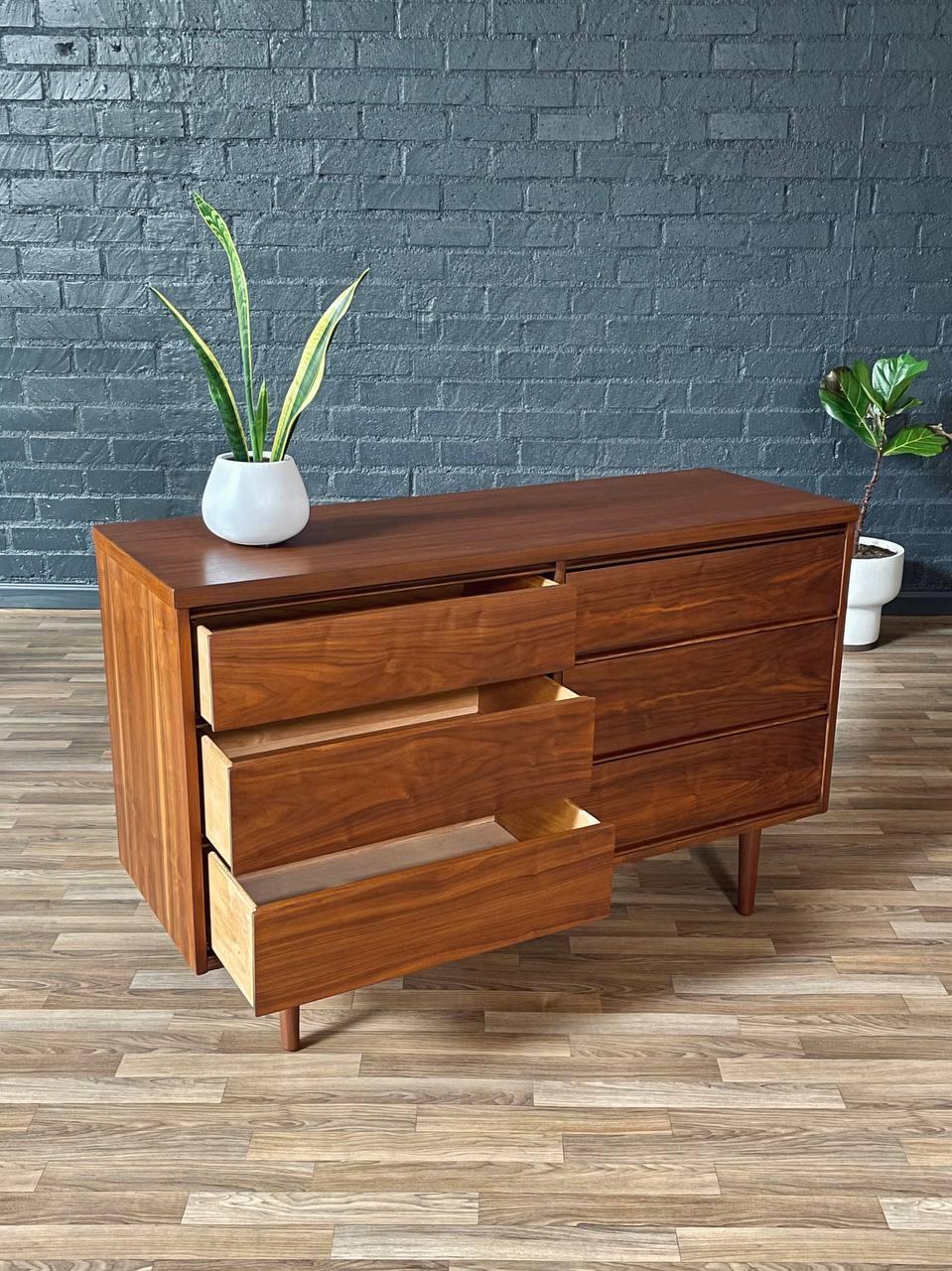 Wooden dresser with a plant on top against a brick wall.