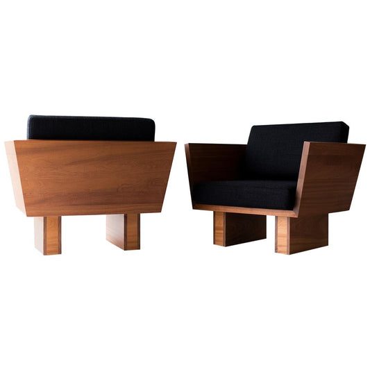 Two modern chairs with wooden frames and black cushions on a white background