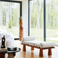 Modern living room with a wooden bench and white cushions, large windows showing a forest view.