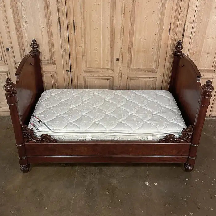 Wooden bed with a mattress against a wooden paneled wall.