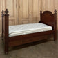 Wooden bed with a mattress against a wooden paneled wall.