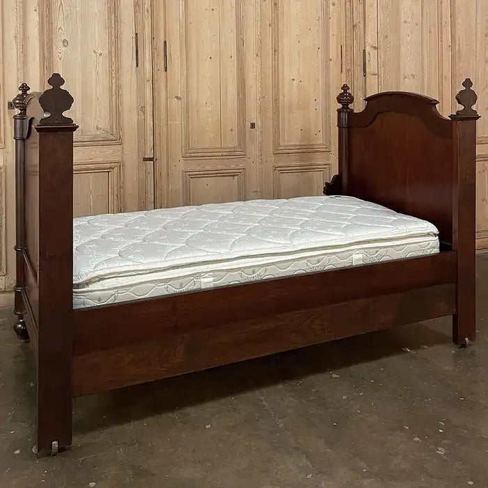 Wooden bed with a mattress against a wooden paneled wall.